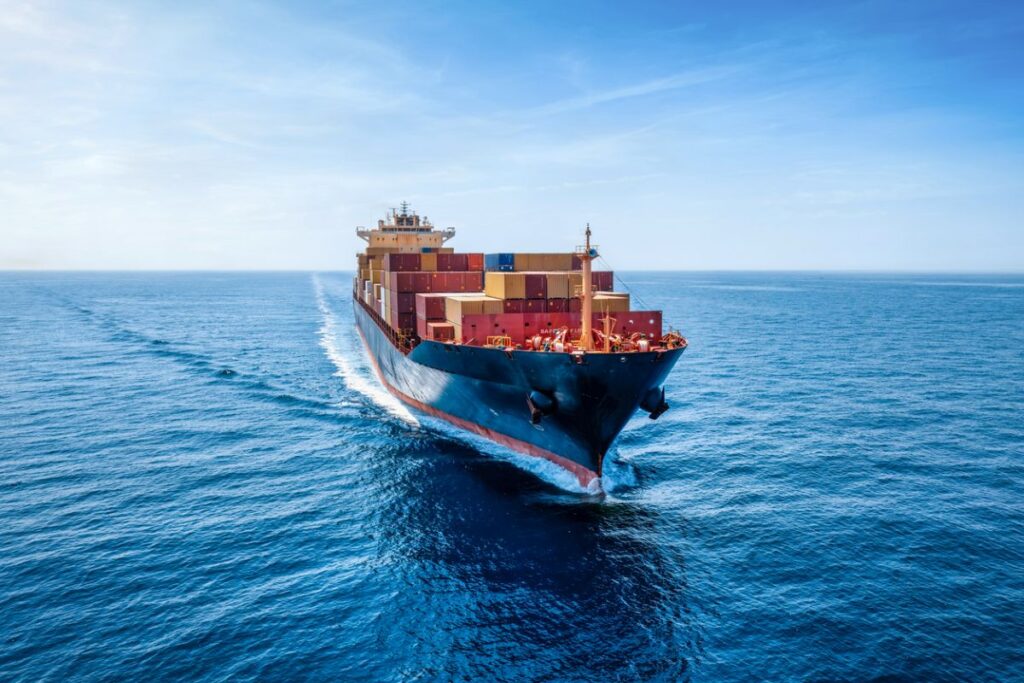 Trump China tariffs — container ship at dusk near a skyline with unbranded cranes and stacks of boxes