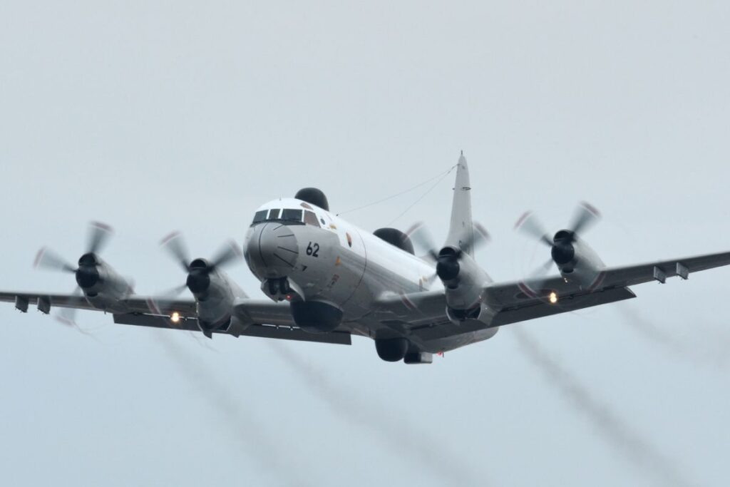 Trump military strategy — U.S. patrol aircraft shadows a dark semi-submersible at sea during a bright midday pass